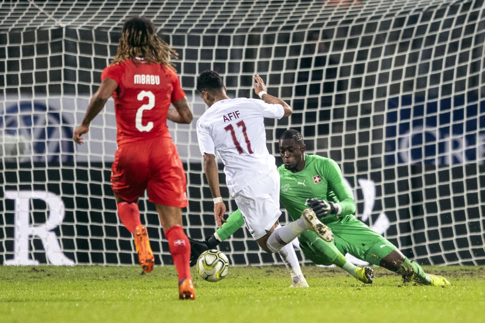 Qatar's Akram Afif, center, scores his side's opening goal past Switzerland's Kevin Mbabu, left, and goalkeeper Yvon Mvogo during an international friendly soccer match between Switzerland and Qatar at the Cornaredo stadium in Lugano, Switzerland, Wednesday, Nov. 14, 2018. (Ennio Leanza/Keystone via AP)