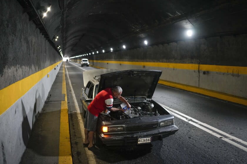 A man tries to cool down his overheating car by pouring water into the radiator, in one of the tunnels of the road that connects La Guaira with Caracas, Venezuela, Tuesday, April 19, 2022. Drivers try to coax a little more life out of aging vehicles in a country whose new car market collapsed and where few can afford to trade up for a better used one. (AP Photo/Matias Delacroix)