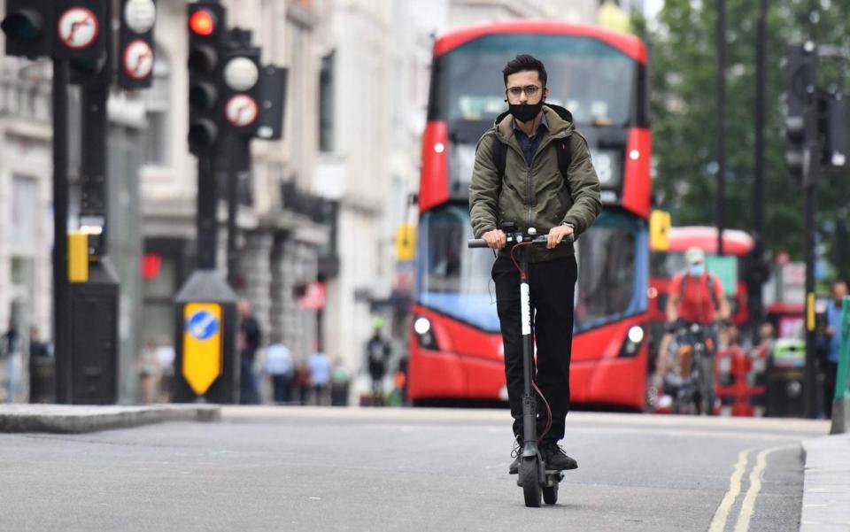 A man rides an e-scooter down Oxford St in central London - AFP