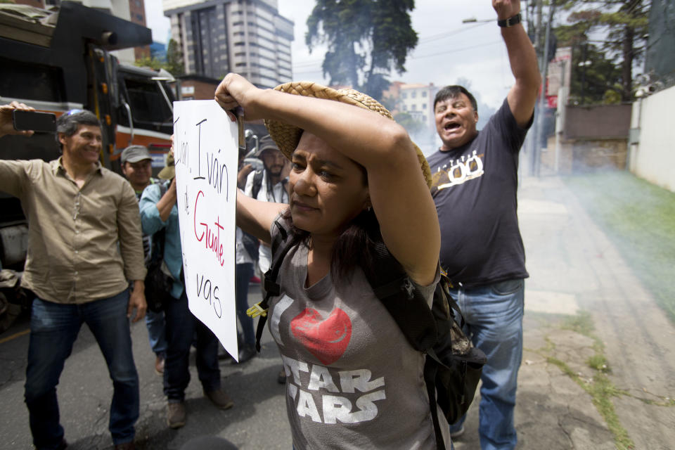 Supporters of Commissioner Ivan Velasquez, front, holds a sing as anti-CICIG protestor, back, fires fireworks in front of the United Nations International Commission Against Impunity, CICIG, headquarters in Guatemala City, Friday, Aug. 31, 2018. Guatemala president Jimmy Morales says he is not renewing mandate of U.N.-sponsored commission investigating corruption in the country. (AP Photo/Moises Castillo)