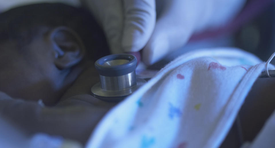 Newborn baby with blanket over it and closeup of stethoscope on its back.