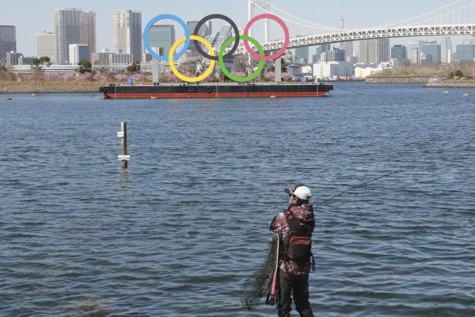 Un pescador disfruta de la pesca con los anillos olímpicos flotando en el agua en Tokio, martes 23 de febrero de 2021