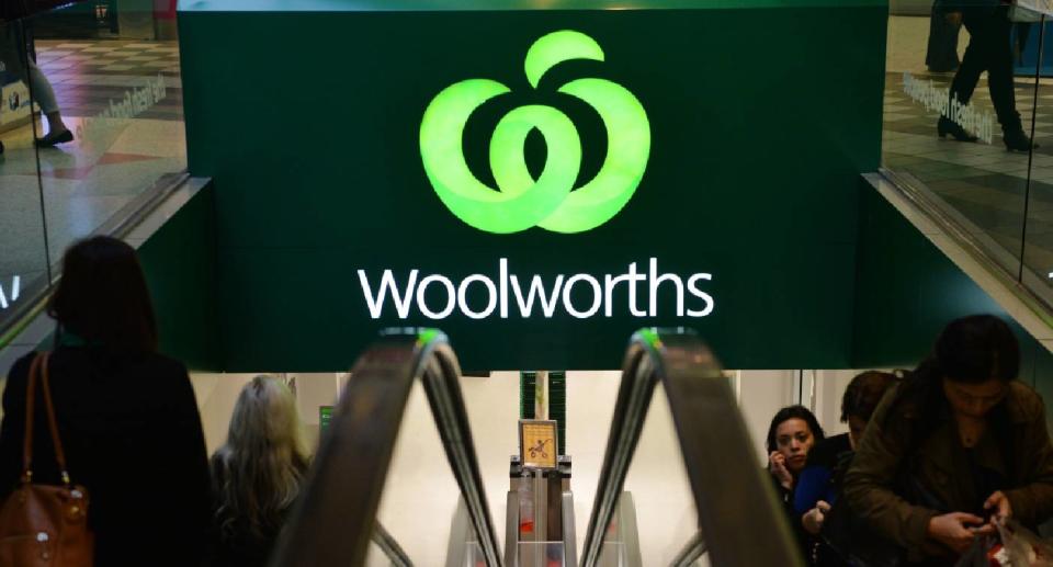 Customers on an escalator in front of a Woolworths store sign