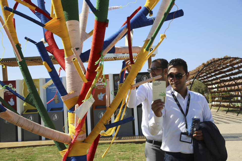 Visitors to the Green Zone read notes posted on an artificial tree set up for people to hang a written promise of what they will do to help fight climate change, at the COP27 U.N. Climate Summit, in Sharm el-Sheikh, Egypt, Friday, Nov. 18, 2022. (AP Photo/Thomas Hartwell)