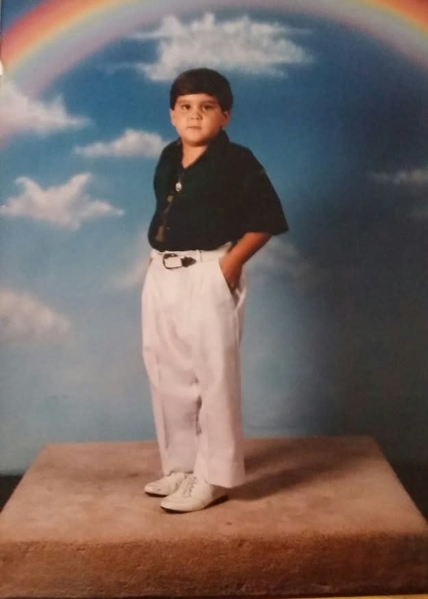 A child standing on a pedestal, with their hands in their pants pocket, with a rainbow design behind them