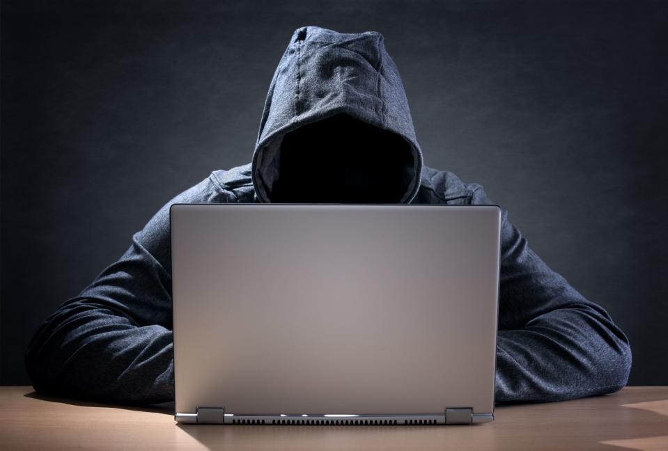 A cyber criminal wearing a hoodie and using a laptop.