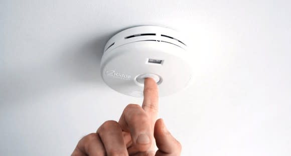 A person pushing the test button on a smoke alarm.