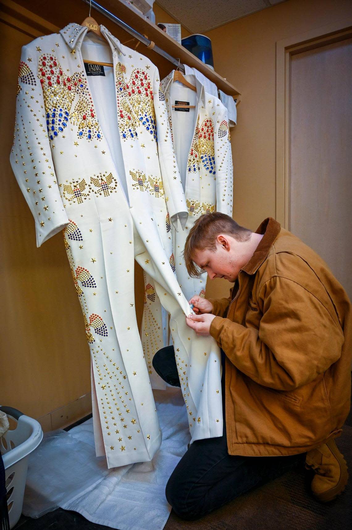 Jak Bush, an assistant stage technician, uses a toothbrush to remove a tiny spot from the Aloha white jumpsuit that will be worn by Trevino during the show. Bush was working on the suit about two hours before Trevino took the stage.