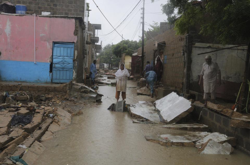 Local residents gather beside their damaged houses caused by heavy monsoon rains, in Yar Mohammad village near Karachi, Pakistan, Thursday, Aug. 27, 2020. Pakistan's military said it will deploy rescue helicopters to Karachi to transport some 200 families to safety after canal waters flooded the city amid monsoon rains. (AP Photo/Fareed Khan)