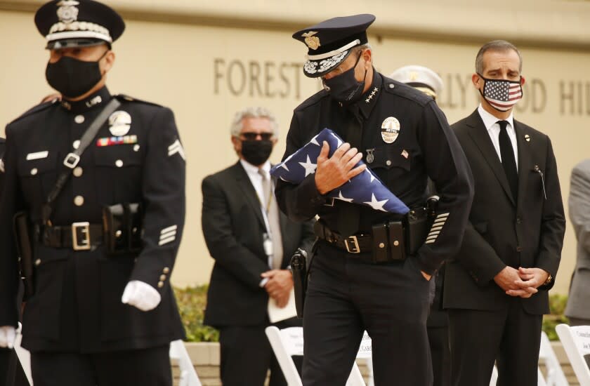 LOS ANGELES, CA - AUGUST 06: Chief of the Los Angeles Police Department Michel R Moore carries the United States flag to present to Megan Flynn, domestic partner who is pregnant with twins of LAPD Officer Valentin Martinez, the agency's first sworn employee to die of complications from the COVID-19. The social distance memory service was held at Forest Lawn Hollywood Hills' Hall of Liberty this morning. Martinez was a 13-year veteran of the department and is presumed to have contacted the virus on duty. He was 45 when he died on July 24, 2020, leaving behind his mother, Maria Martinez, his siblings and his domestic partner, Megan Flynn, who is pregnant with their twins. Los Angeles on Thursday, Aug. 6, 2020 in Los Angeles, CA. (Al Seib / Los Angeles Times)