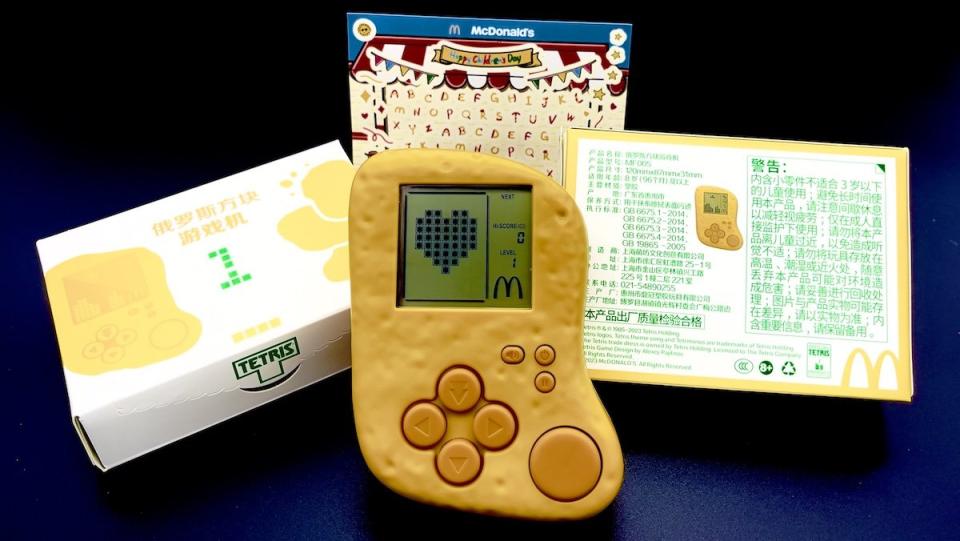 A handheld Tetris device shaped like a McNugget on display with its box, stickers, and bag from McDonald's China