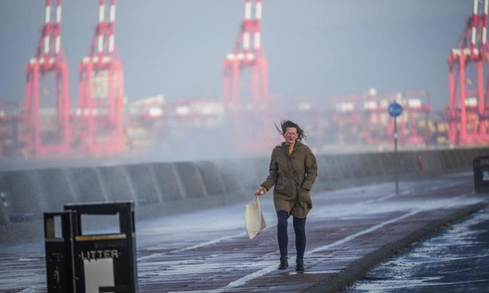 A woman tries to avoid sea spray whipped up by wind and waves in New Brighton, Merseyside, as the UK readies for the arrival of Storm Barra.