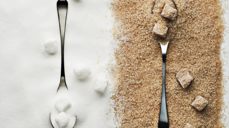 Overhead white sugar and brown sugar spread side by side with sugar lumps and spoons