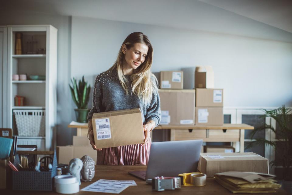 Person in office holding box and looking at laptop.