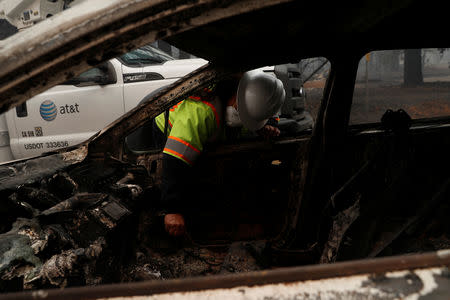 An AT&T worker sifts through a friend's burned car during the Camp fire in Paradise, California, U.S. November 10, 2018. REUTERS/Stephen Lam