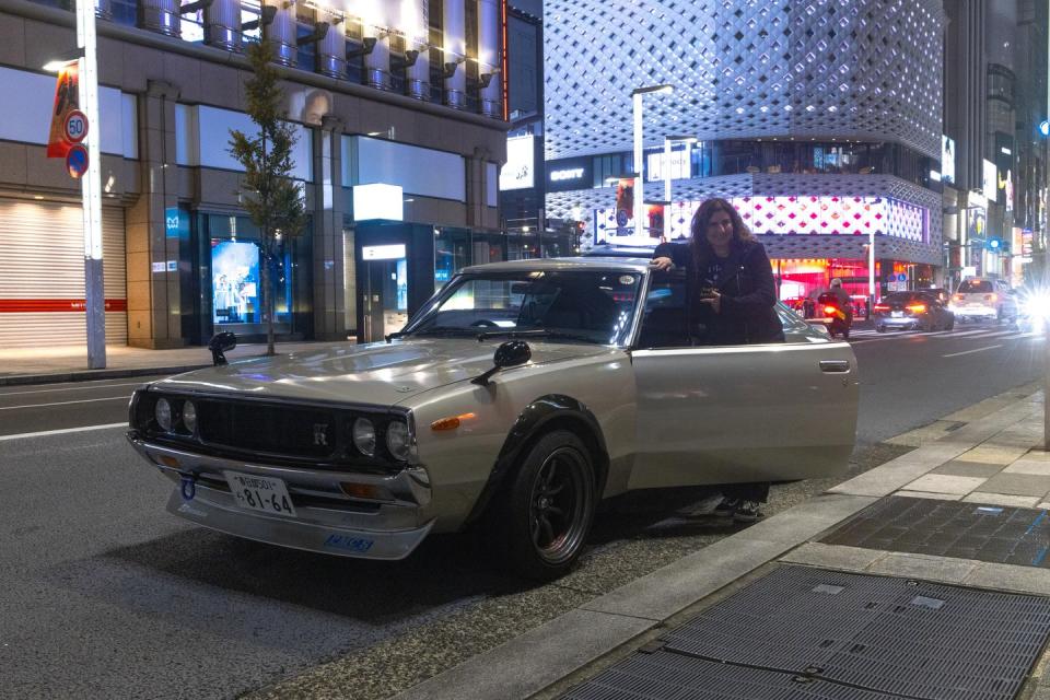 a person standing next to a car on a street with buildings in the background