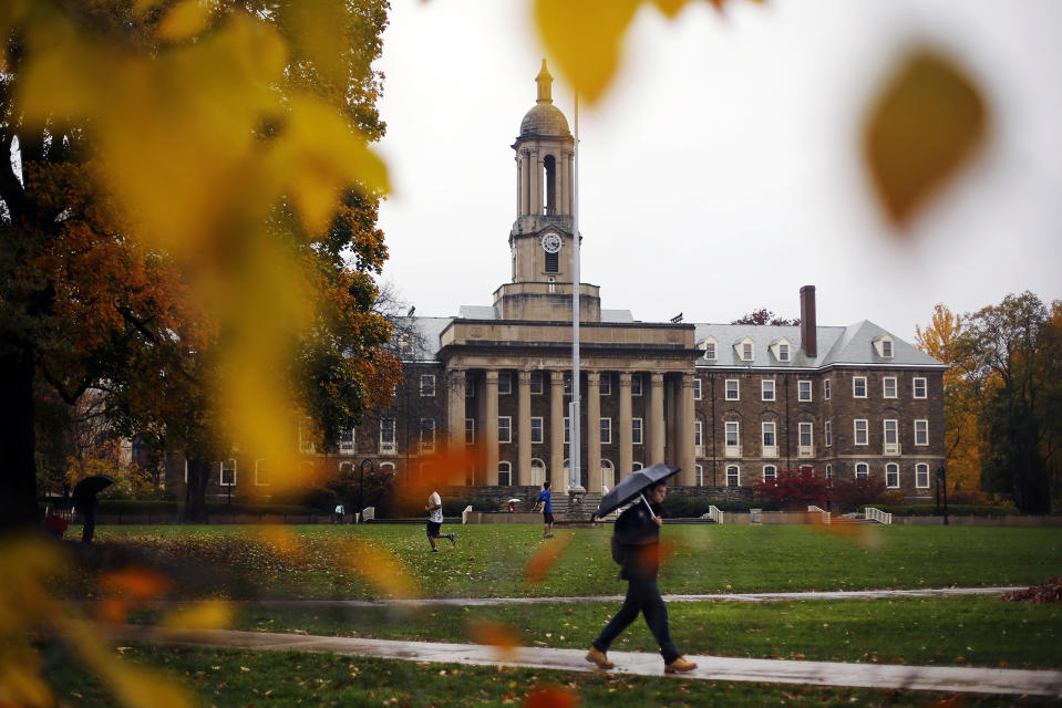 FILE - In this Oct. 28, 2015 file photo, a Penn State student walks in the rain past Old Main on the Penn State main campus in State College, Pa. Lawmakers are trying to stop 144 cities across the U.S. from losing their designations as “metropolitan areas” because the federal government is upgrading the standard from a minimum of 50,000 residents in its core to a minimum of 100,000 people. State College is among the cities at risk of losing the designation. (AP Photo/Gene J. Puskar, File)