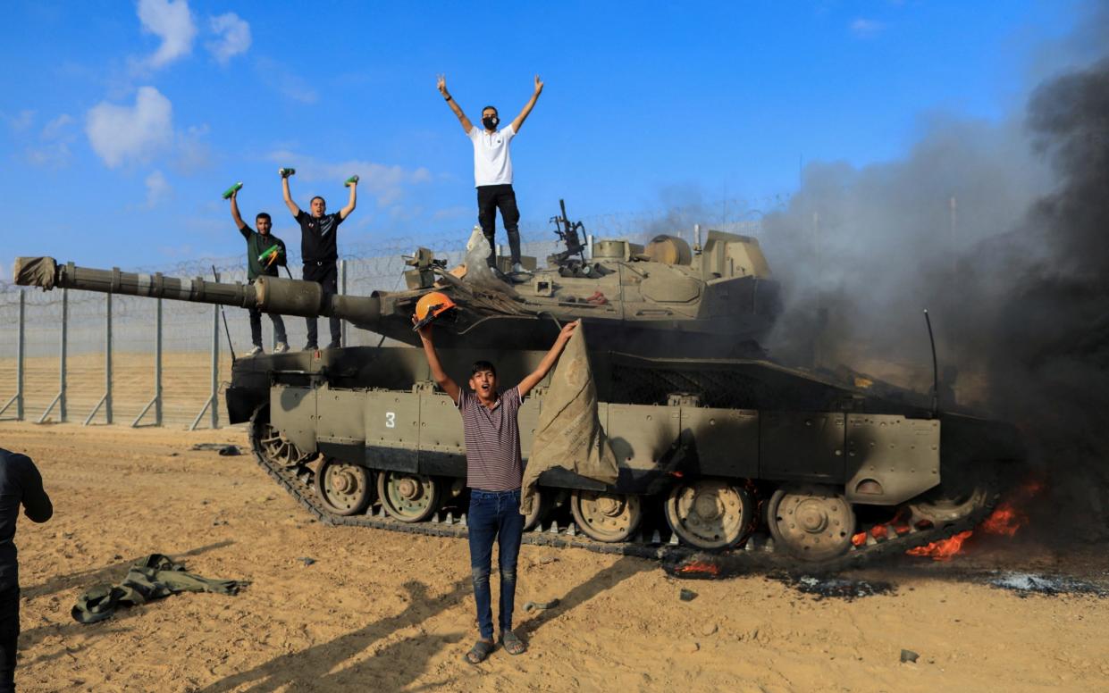 Palestinians celebrate as an Israeli tank burns on the border on Oct 7