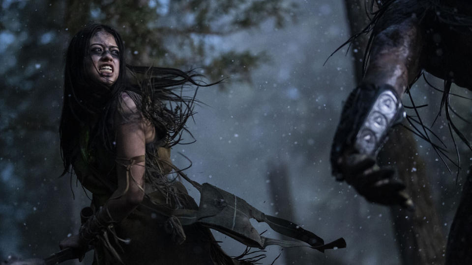 a woman in leather clothing fights a dreadlocked alien in a forest