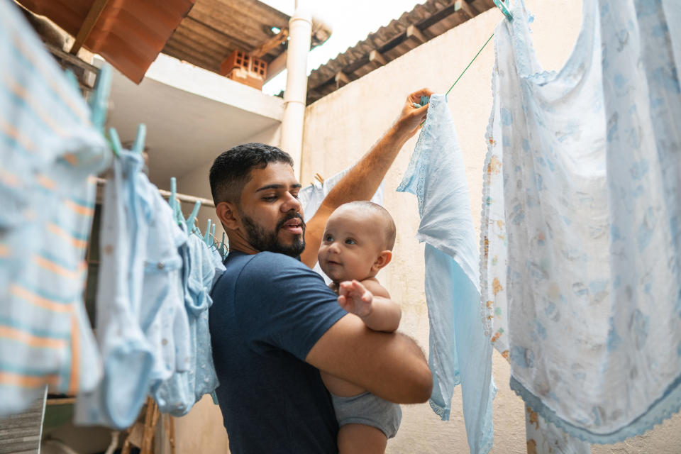 Man holding a baby while hanging laundry on a clothesline