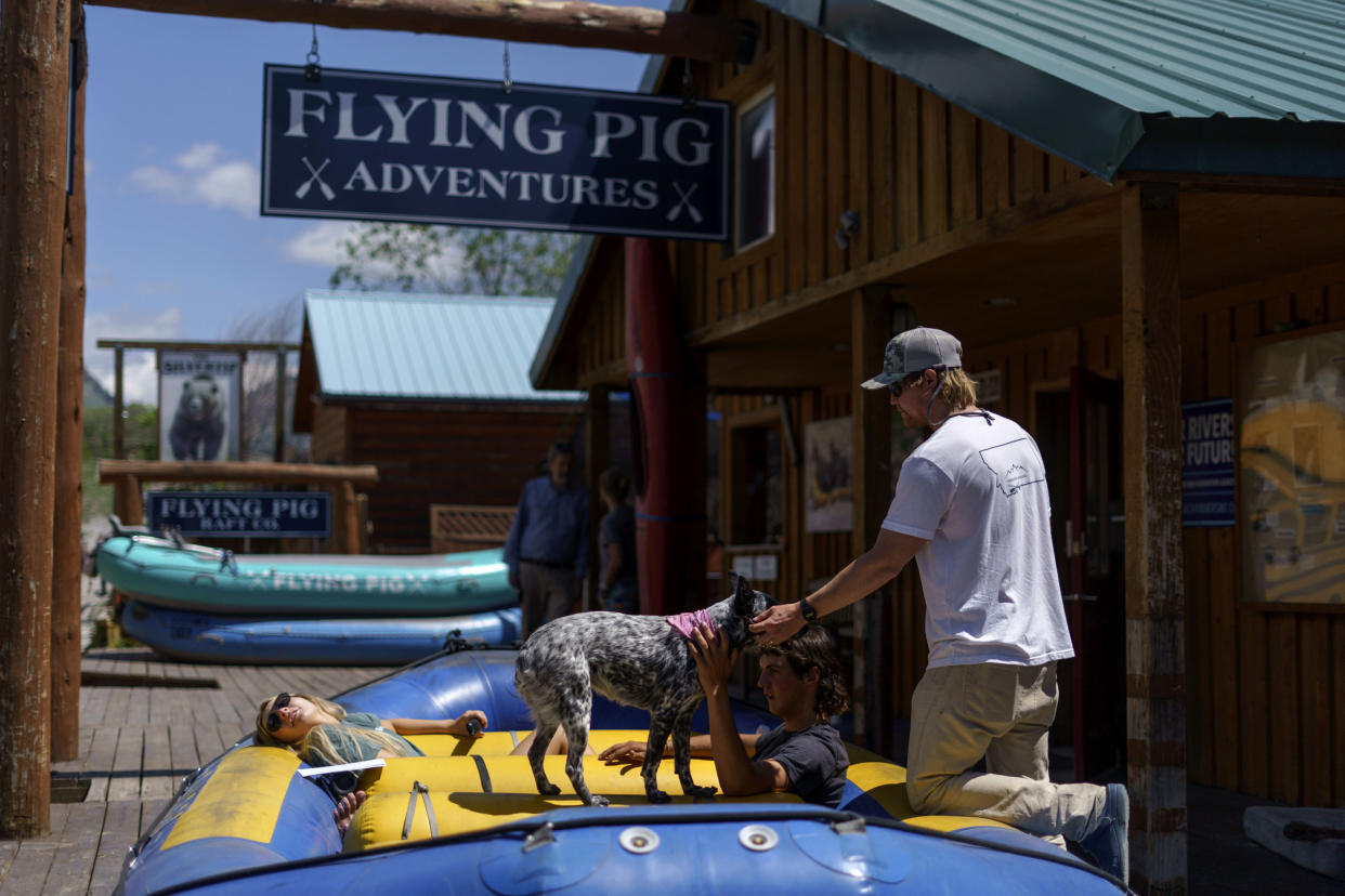 Patrick Sipp, co-owner of Flying Pig Adventures, pets his dog, Bonnie, as employees Jackson Muller, right, and Christie Davis sit in a raft while Yellowstone National Park is closed due to historic flooding in Gardiner, Mont., Wednesday, June 15, 2022. "We're definitely a resilient company, we've got a very tough crew," Sipp said. "But it's devastating. You just hate seeing stuff like that in the community. We're just hoping that we can get back out there relatively soon." (AP Photo/David Goldman)