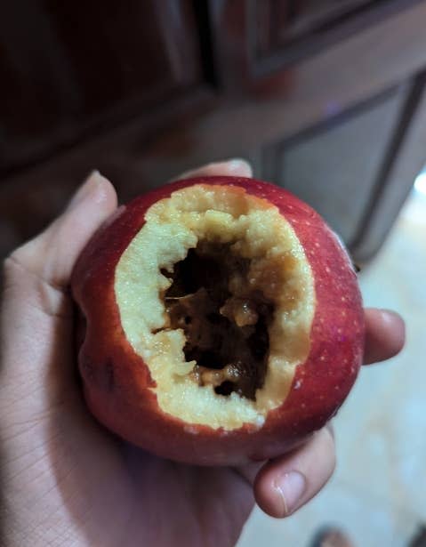 A hand holding an apple with a large, deep bite taken out of it, revealing a brown, decayed core.