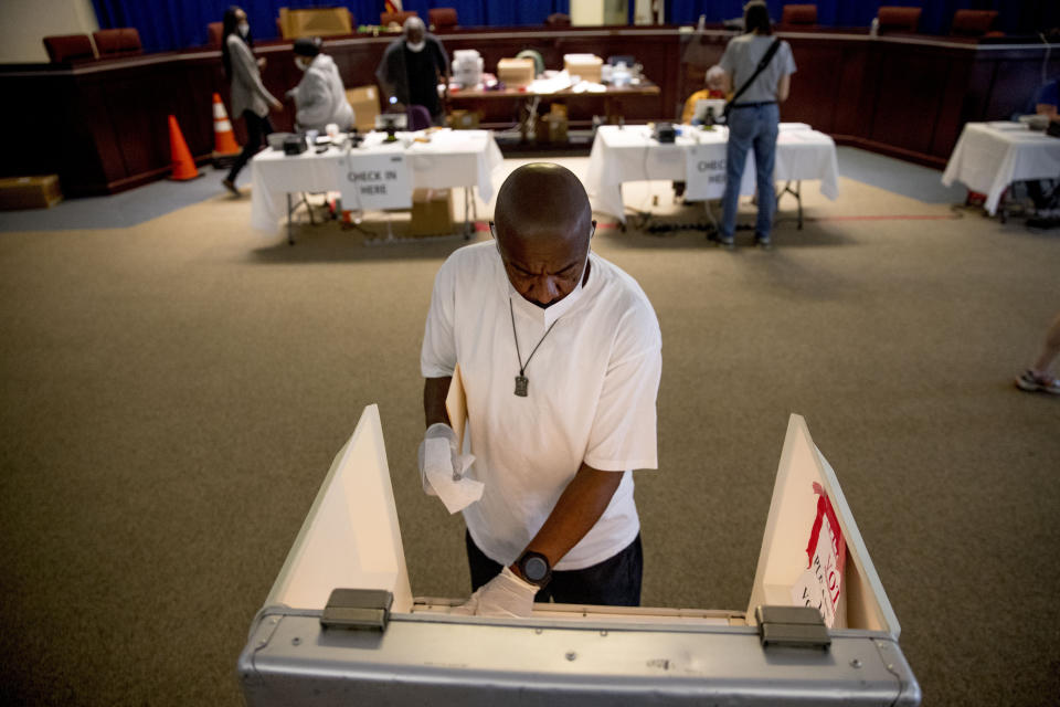 Darren Atkinson wears a mask as he wipes down a voting booth at a voting center during primary voting in Washington, Tuesday, June 2, 2020. (AP Photo/Andrew Harnik)