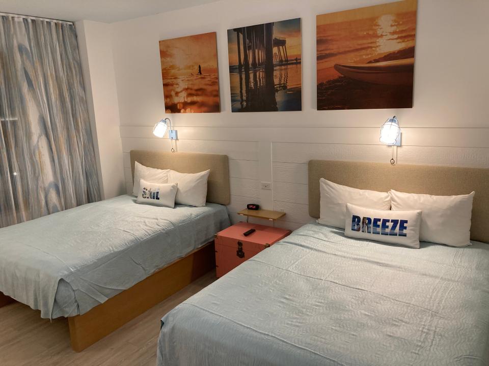 two double beds side by side with lights above them and three photos hanging on wall