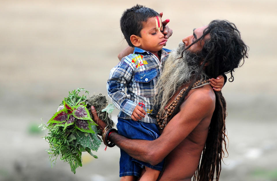 An Indian Hindu Sadhu holds his adopted child, Bajrangi, while walking on the banks of the Sangam, on father's day in Allahabad on June 16, 2013.  AFP PHOTO / SANJAY KANOJIA        (Photo credit should read Sanjay Kanojia/AFP/Getty Images)