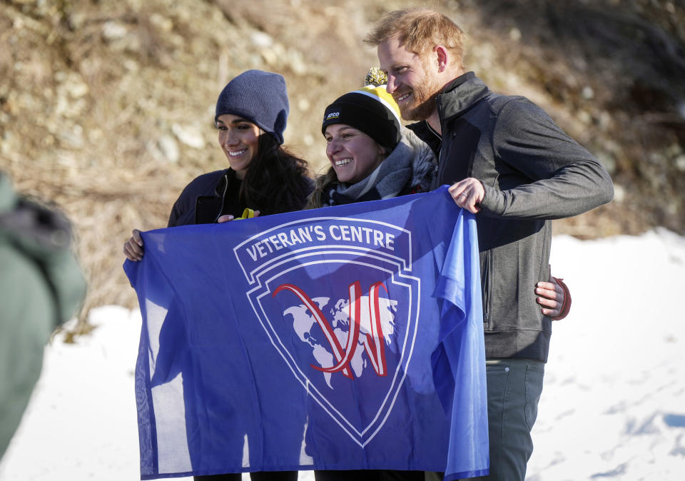 Prince Harry, right, and Meghan Markle, the Duke and Duchess of Sussex, pose with a woman while holding a flag during an Invictus Games training camp, in Whistler, British Columbia, Thursday, Feb. 15, 2024. Invictus Games Vancouver Whistler 2025 is scheduled to take place from Feb. 8 to 16, 2025 and will for the first time feature winter sports. (Darryl Dyck/The Canadian Press via AP)