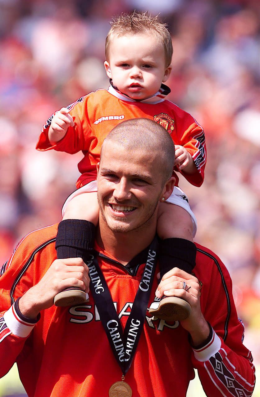 This picture can only be used in the context of an editorial feature. Manchester United's David Beckham carries his son Brooklyn on his shoulders, as his side are crowned FA Carling Premiership Champions after their match against Tottenham Hotspur. * ...at Old Trafford, Manchester. Final score : Manchester United 3, Tottenham Hotspur 1. 22/02/02 David and Victoria Beckham announced that they are expecting their second child in September. (Photo by Phil Noble - PA Images/PA Images via Getty Images)