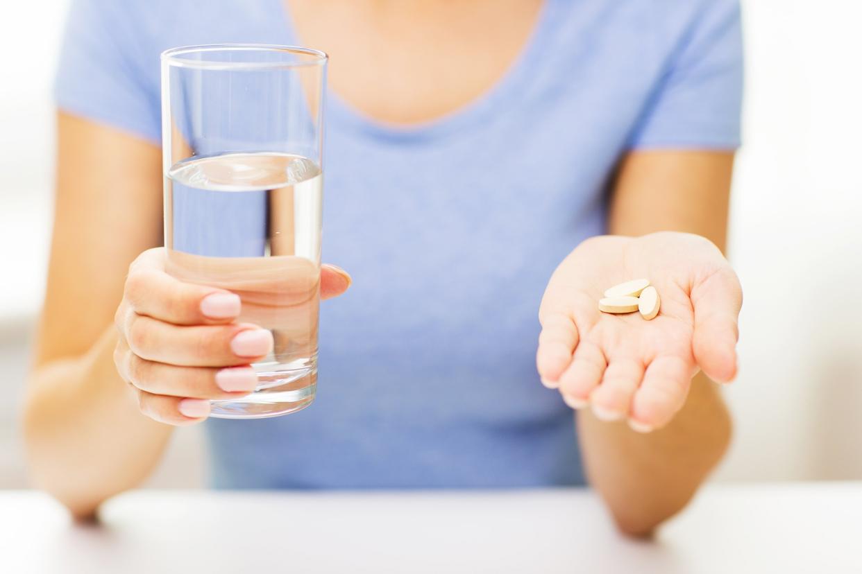 woman hands holding pills and water glass at home