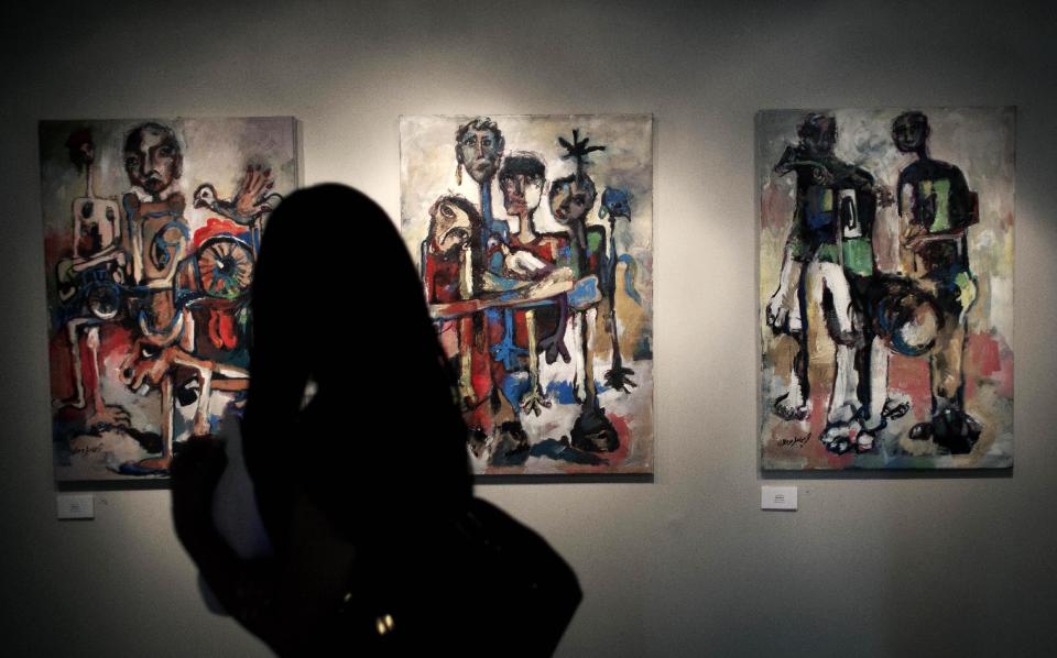 In this photo taken Saturday, May 10, 2014, a woman looks at a series of three acrylic on canvas paintings named Hamamah, by Palestinian artist Ismail Dahlan, during an art exhibition "Traces, a testimony to memory," displaying over forty Palestinian artists work from Gaza, in the West Bank city of Ramallah. Fifty-three paintings and two sculptures by 45 artists have gone on display in the West Bank city of Ramallah, said Haneen Qatamesh, a spokeswoman for one of the sponsors, the Palestinian company PADICO. Since Saturday's opening, 12 works have been sold for prices ranging from $850 to $9,000, she said. (AP Photo/Nasser Nasser)