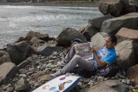 A man reads a newspaper next to the Pacific Ocean on the coast of Lima, Peru, Friday, June 26, 2020, amid the coronavirus pandemic. (AP Photo/Rodrigo Abd)