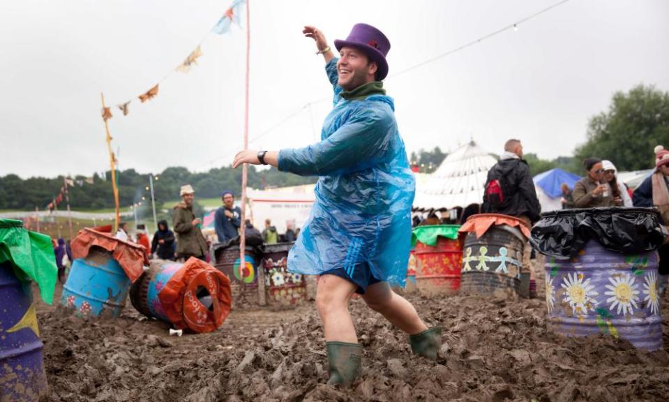 Man in a top hat and a plastic mac dances ankle-deep in mud at Glastonbury 2016