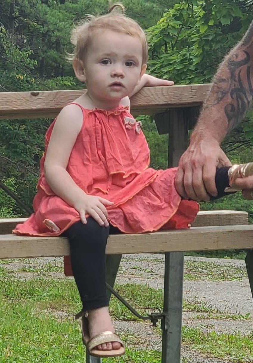 Two-year-old Nevaeh Muley sitting on park table wearing black leggings and pink dress outside against trees
