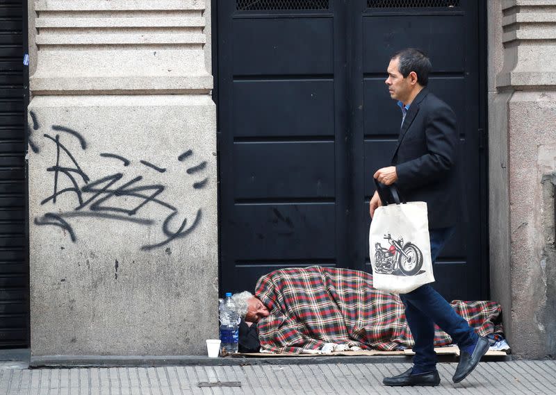 A pedestrian walks past a homeless man sleeping near the National Congress, as Argentines struggle amid rising inflation, in Buenos Aires