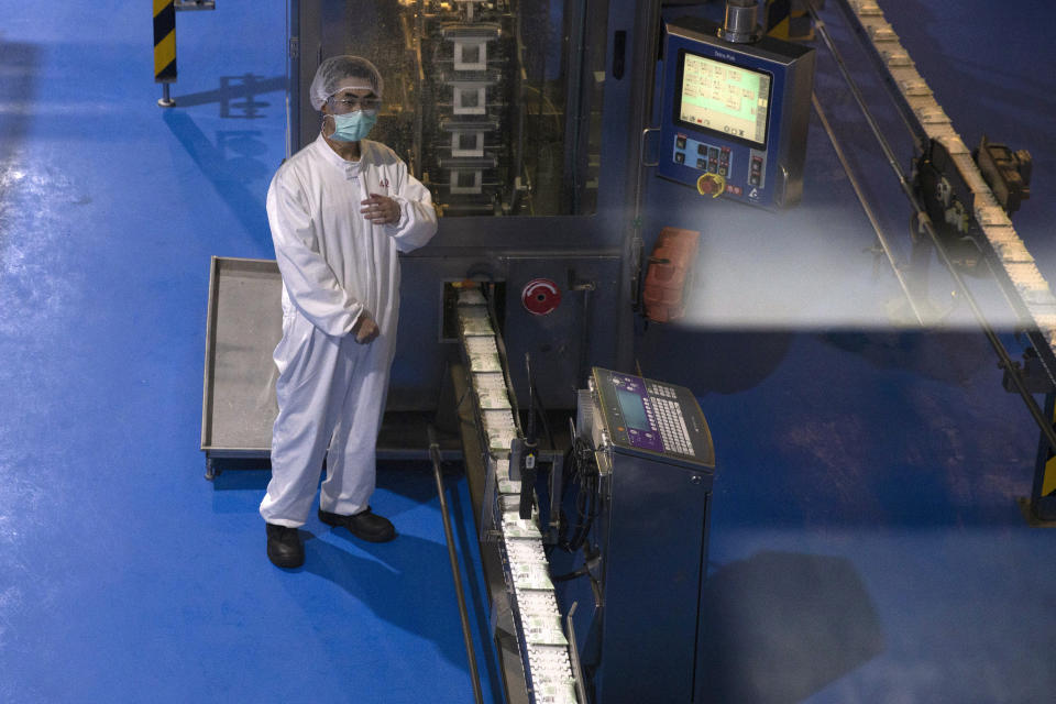 In this Thursday, Feb. 27, 2020, photo, a worker checks yogurt coming off the production line at the Mengniu dairy factory in Beijing. Reporters were invited to China Mengniu Dairy Co. Ltd. this week to be shown how companies are reviving after anti-virus measures shut down most of the world's second-biggest economy. White space at right is reflection of the glass window. (AP Photo/Ng Han Guan)