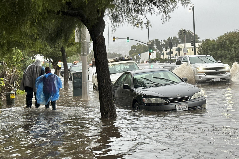 Pedestrians walk on a flooded sidewalk as rain comes down, Thursday, Dec. 21, 2023 in Santa Barbara, Calif. (AP Photo/Eugene Garcia)