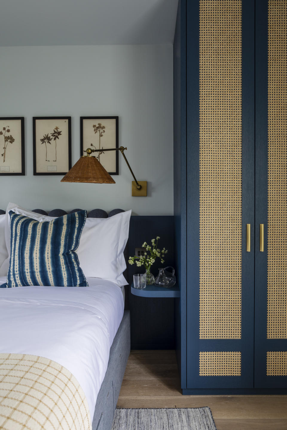 blue bedroom with blue and rattan custom wardrobes and side table, rattan wall light, stripe cushion, artwork on wall