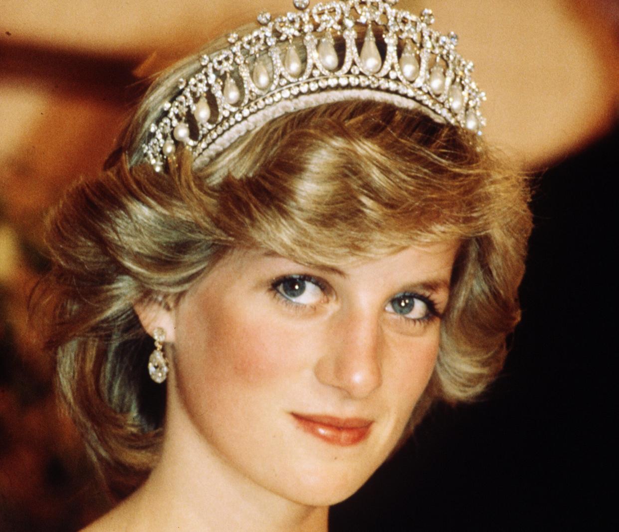 Diana, Princess of Wales, wearing a cream satin dress by Gina Fratini with the Queen Mary Cambridge Lover's Knot Tiara and diamond earrings attends a banquet on April 29, 1983 in Auckland, New Zealand