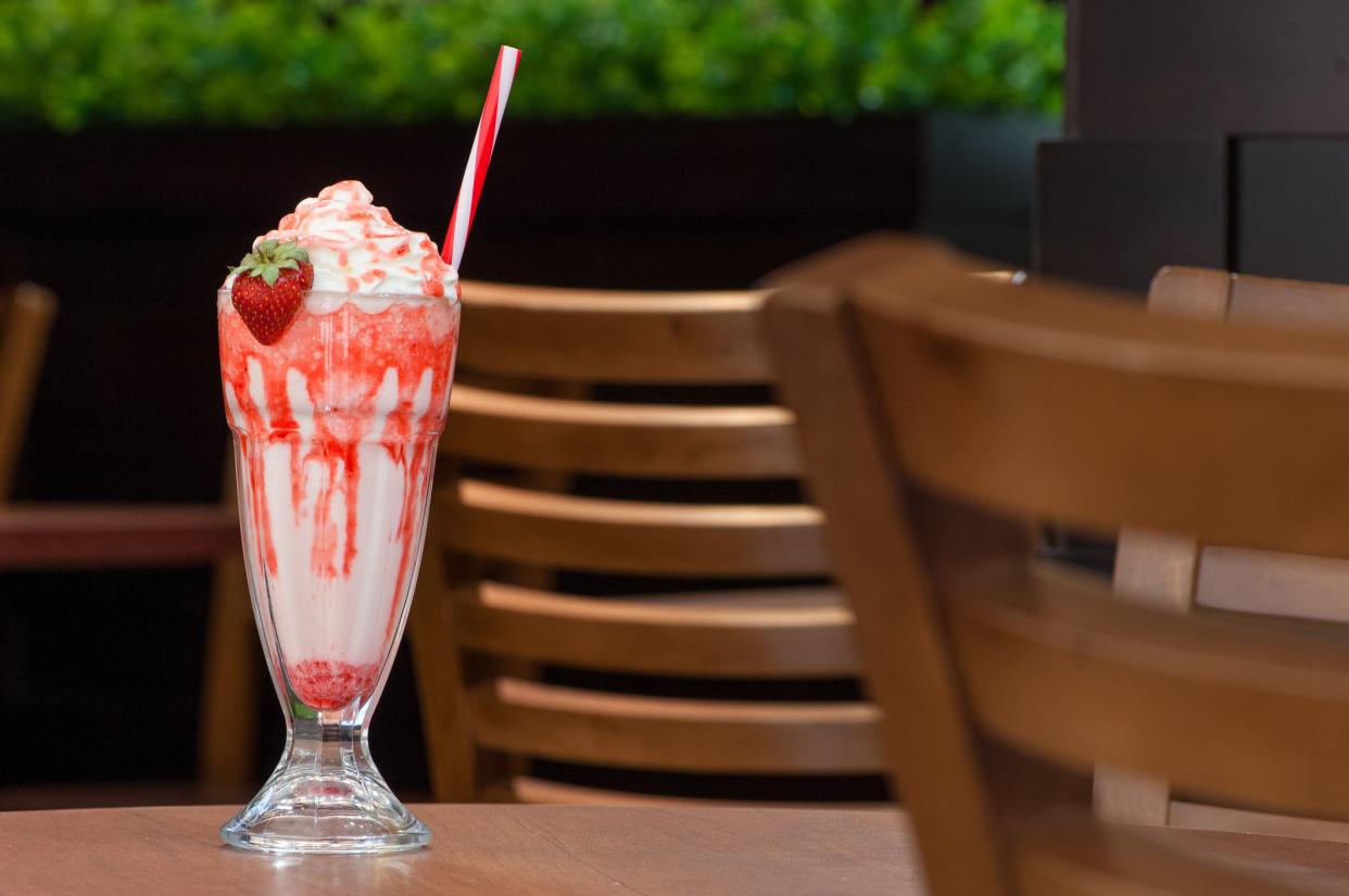 cold drink with a straw and strawberries in a transparent glass on the table on the background of chairs