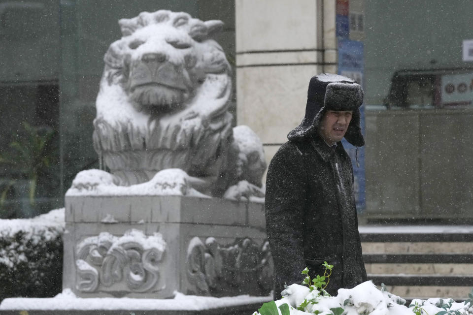 A security guard stands near a stone lion with a covering of snow in Beijing, China, Sunday, Nov. 7, 2021. An early-season snowstorm has blanketed much of northern China including the capital Beijing, prompting road closures and flight cancellations. (AP Photo/Ng Han Guan)