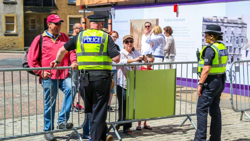 Police Scotland officers chat with citizens across a metal barrier.