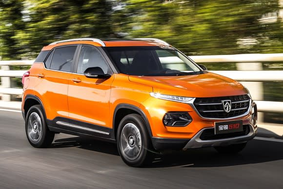 An orange Baojun 510, a compact SUV, at speed on a country road.