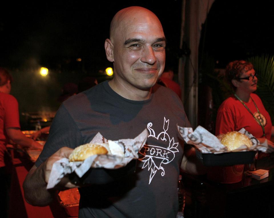 Michael Symon holds his Porky Burgers during the Burger Bash at the Food Network South Beach Wine & Food Festival in Miami Beach, Fka., on Friday, Feb. 24, 2012. (AP photo/Jeffrey M. Boan)