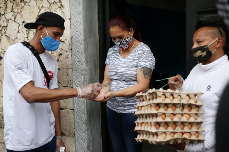 El empleado del restaurante La Chicheria Demente desinfecta las manos de Miryam Tellez, gerente de alojamiento, durante la entrega de alimentos donados, en medio del brote de la enfermedad por coronavirus (COVID-19) en Bogotá, Colombia