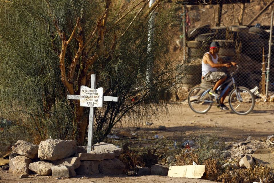 A person rides a bicycle near a cross surrounded by rocks in front of a tree