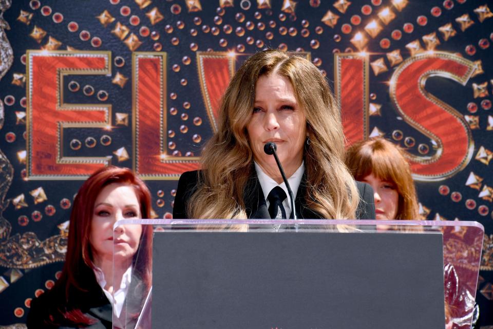 Priscilla Presley, Lisa Marie Presley, and an unidentified woman at an event with an "ELVIS" backdrop. Lisa Marie is speaking at a podium