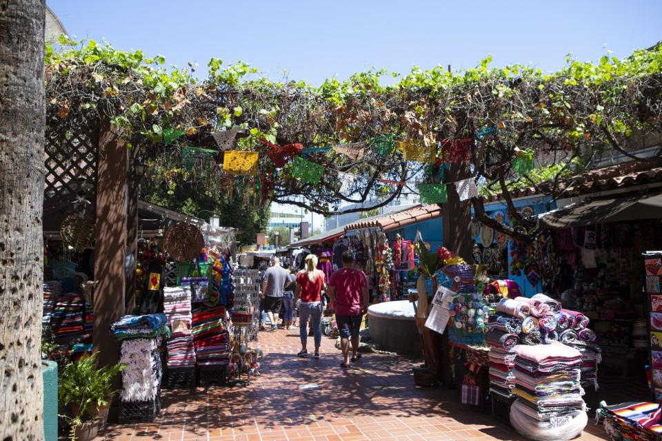 Small storefronts and booths with goods piled high line a brick walkway under colorful paper flags